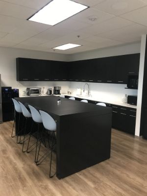 Office break room with black painted cabinets and a black island with white stools