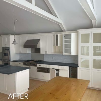 Kitchen after cabinet refinishing, white cabinets and a dark hood under a vaulted beamed ceiling