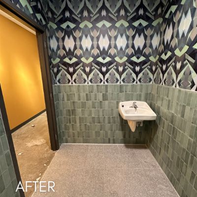 Restroom papered in a bold leaf print above green tile