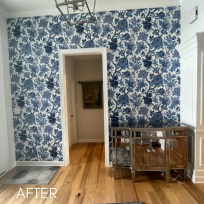 Room papered in a blue and white floral print on bare wood flooring