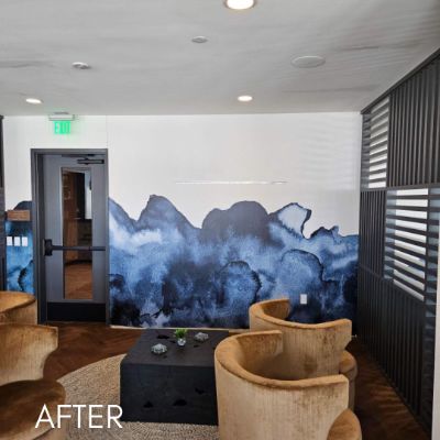 Office lounge with a blue watercolor mountain mural behind low chairs