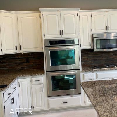 Kitchen after cabinet refinishing, white cabinets and a double wall oven against a dark backsplash
