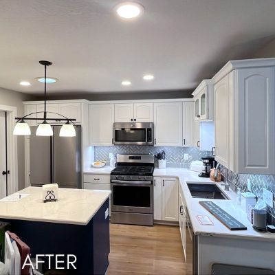 Kitchen after cabinet refinishing, white cabinets and a navy island