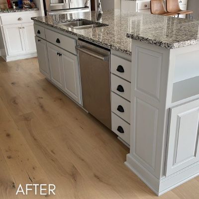 Kitchen cabinets refinished white with black hardware, beside a stainless dishwasher