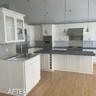 Kitchen after cabinet refinishing, white cabinets and dark countertops under a vaulted ceiling