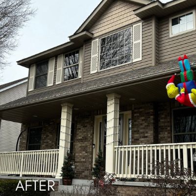 Two-story house with brown shake siding, white porch rails and brick skirting