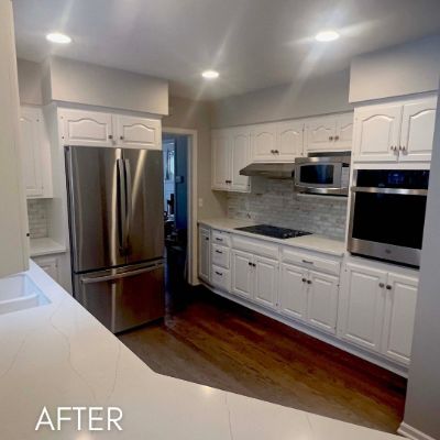 Kitchen after cabinet refinishing, white arched cabinet doors around stainless appliances