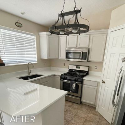 Kitchen after cabinet refinishing, white cabinets below a wrought iron pot rack