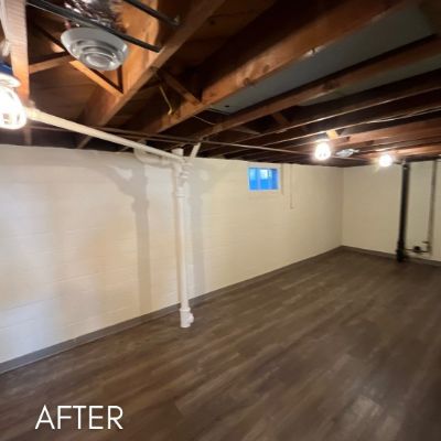 Basement after painting, white walls and exposed joists above a vinyl floor