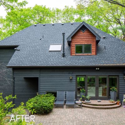 House in slate gray siding with a cedar-clad dormer above a paved patio