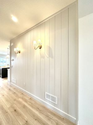 Hallway lined with white vertical shiplap paneling and brass wall sconces