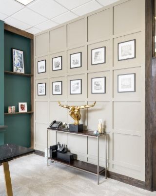 Office wall in beige grid paneling hung with framed prints, beside a dark green painted alcove