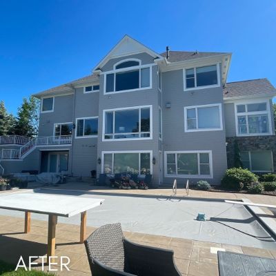Three-story house in gray siding with white trim, above a paved terrace