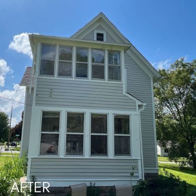 Front elevation of a house in pale green siding with banked windows
