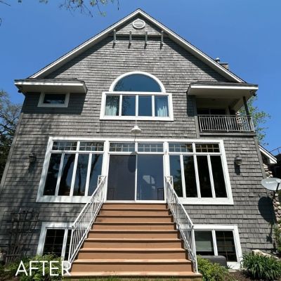 Lakeside shingled house in gray with white window trim above a wooden stair