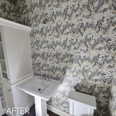 Powder room papered in a blue and white tree print above a pedestal basin