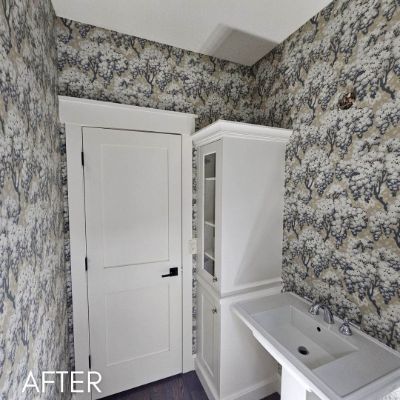 Powder room papered in a blue tree print beside a white linen cupboard