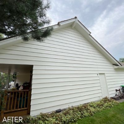 Gable end of a house in cream siding above a shrub border