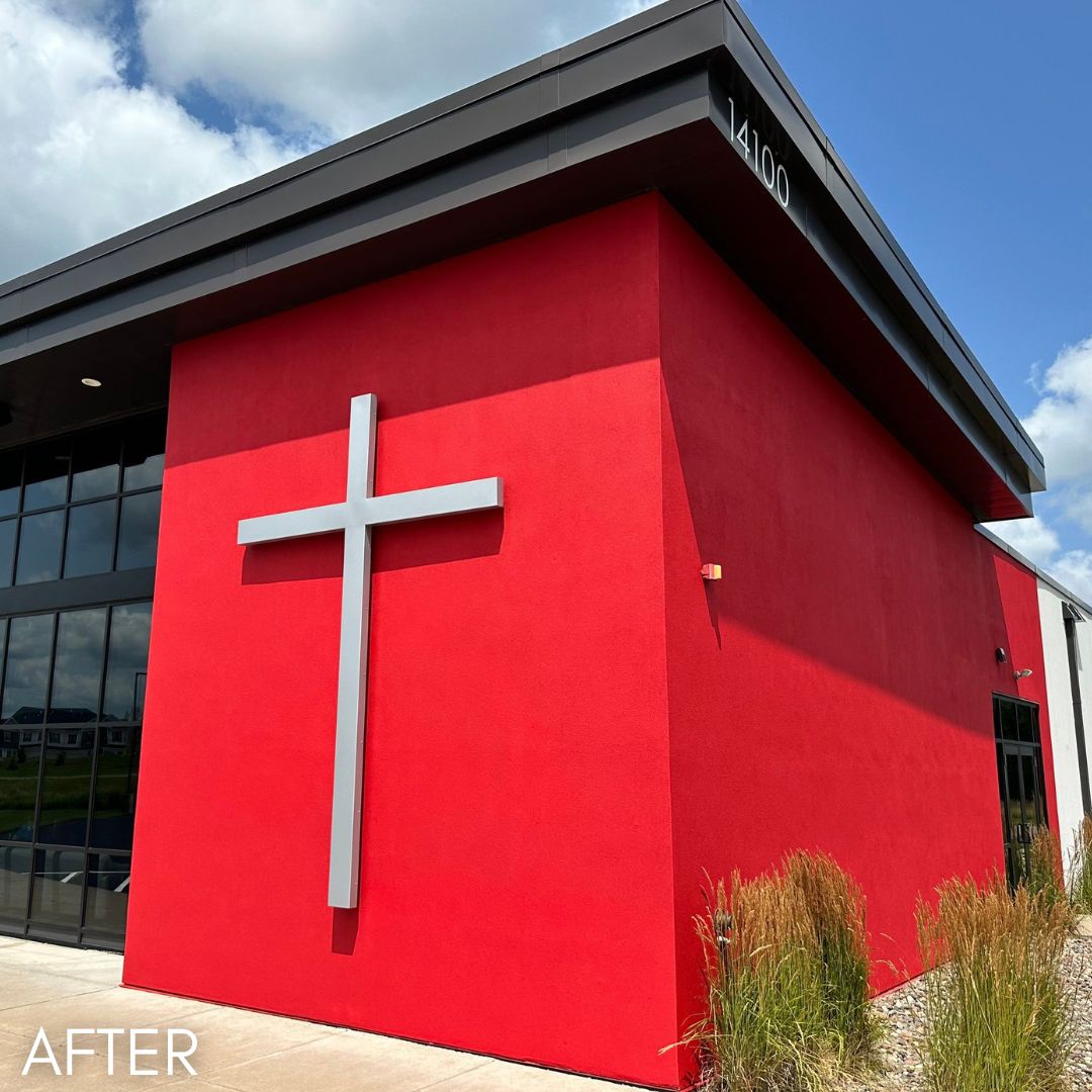 Corner of a church painted bright red, with a white cross on the end wall