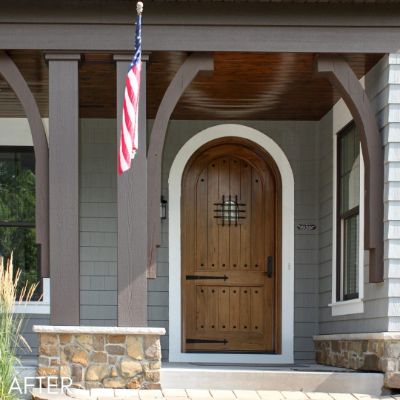 Arched wood front door under a covered porch with stone columns
