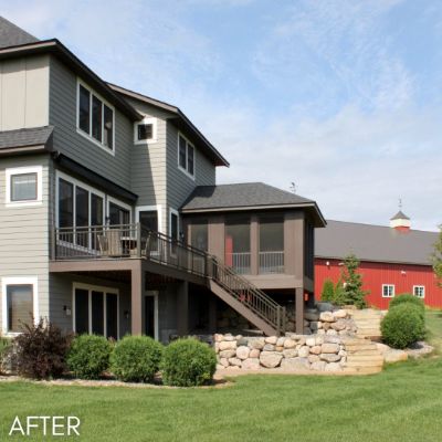 Three-story house in gray siding with a walkout deck, a red barn behind it