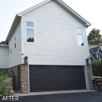 Garage wing in white siding with a dark brown garage door and stone base