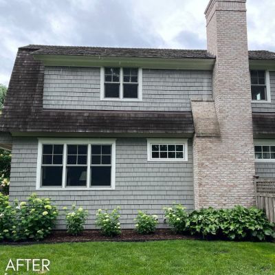 Gambrel-roofed house in gray shingle siding with a brick chimney