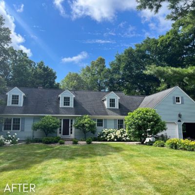 Cape Cod house in pale green with white dormers behind a mown lawn