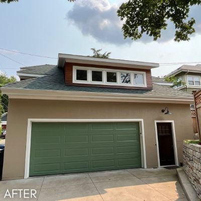 Garage in tan stucco with a sage green door and a cedar-clad dormer