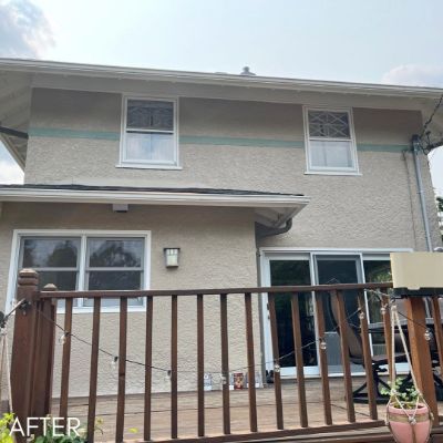 House in tan stucco with white window trim beside a wooden deck rail