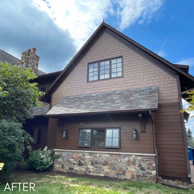 Shingled house in tan above dark stained siding and a stone base