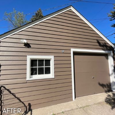 Detached garage in brown siding with white window trim