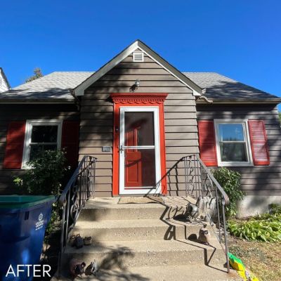Bungalow in tan siding with a bright red front door and matching shutters