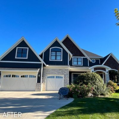 Two-story house in navy siding with white trim and stone-faced garages