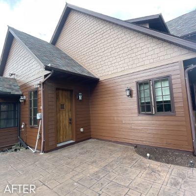 House in stained cedar siding with a wood front door above a stamped patio