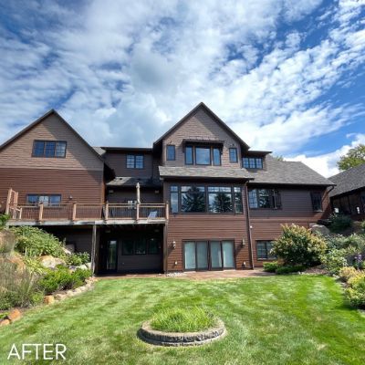 Large shingled house in brown with a walkout deck above a planted garden