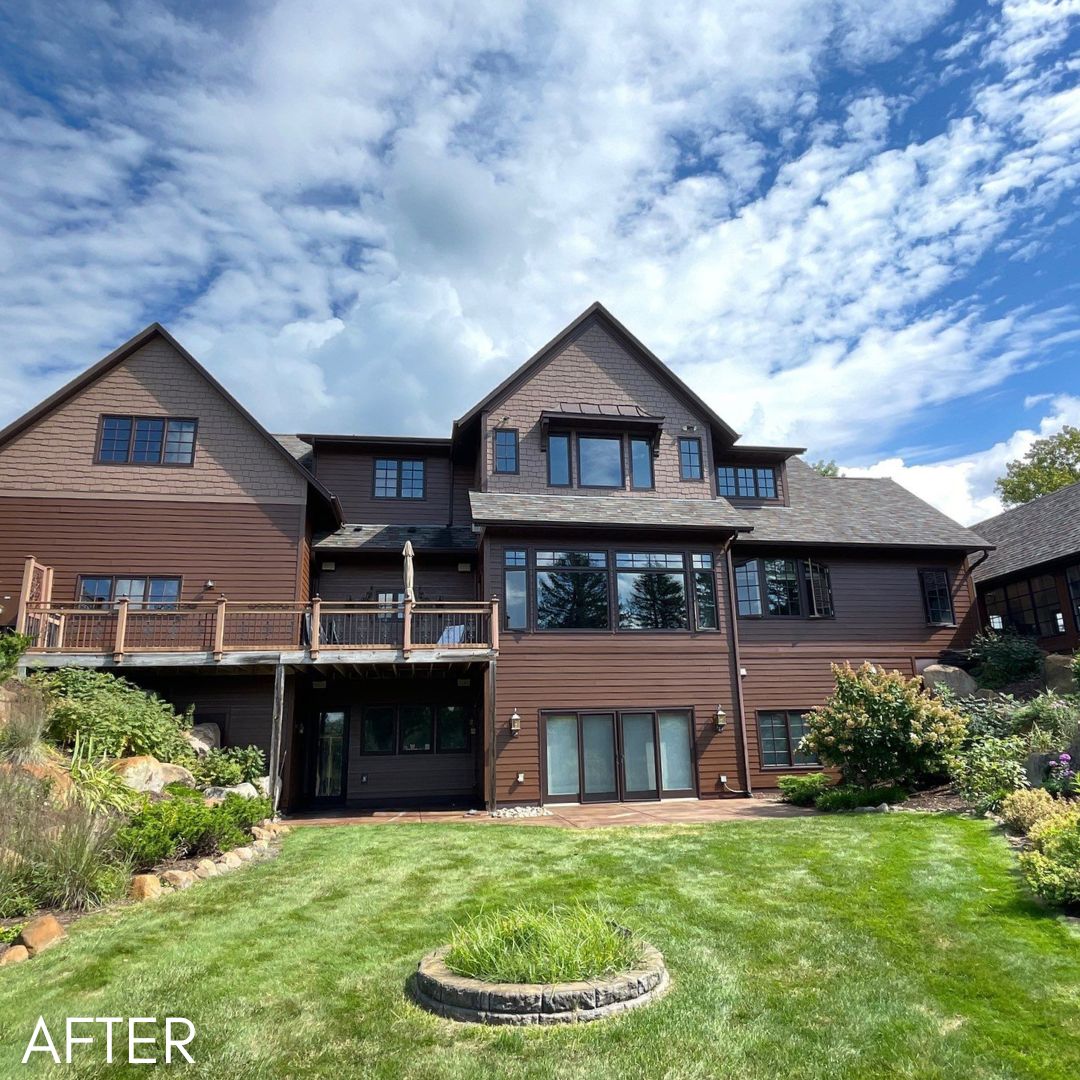 Large shingled house in brown with a walkout deck above a planted garden