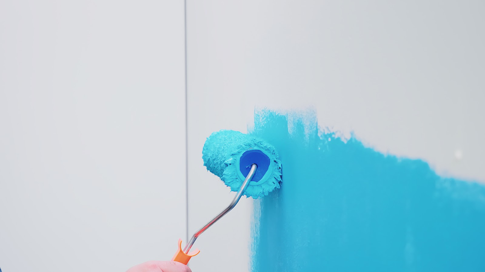 A roller laying a band of bright turquoise paint across a white wall