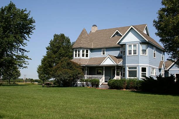 Blue clapboard farmhouse with a wraparound porch, standing in open country