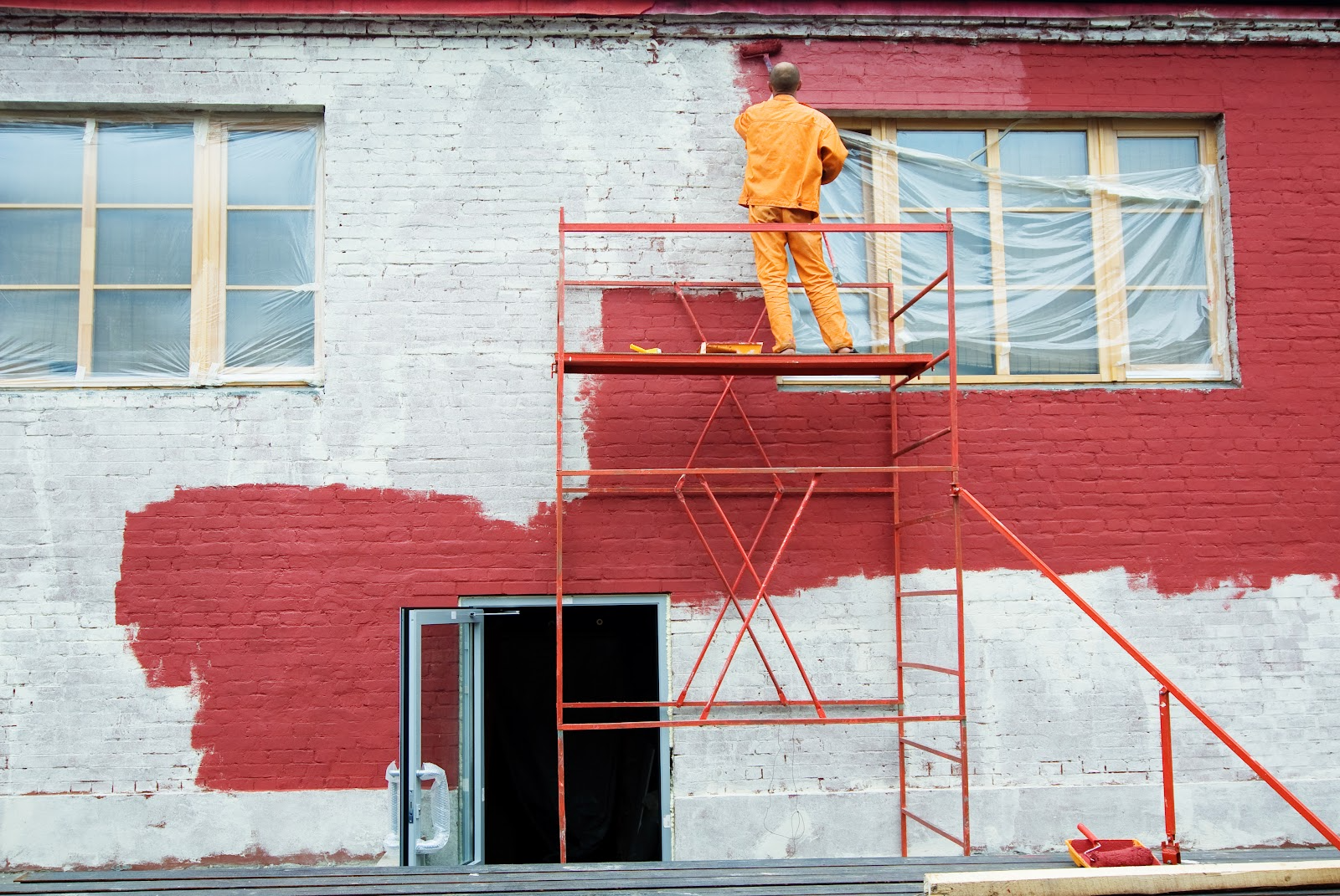 Painter on scaffolding rolling deep red paint onto a brick commercial building