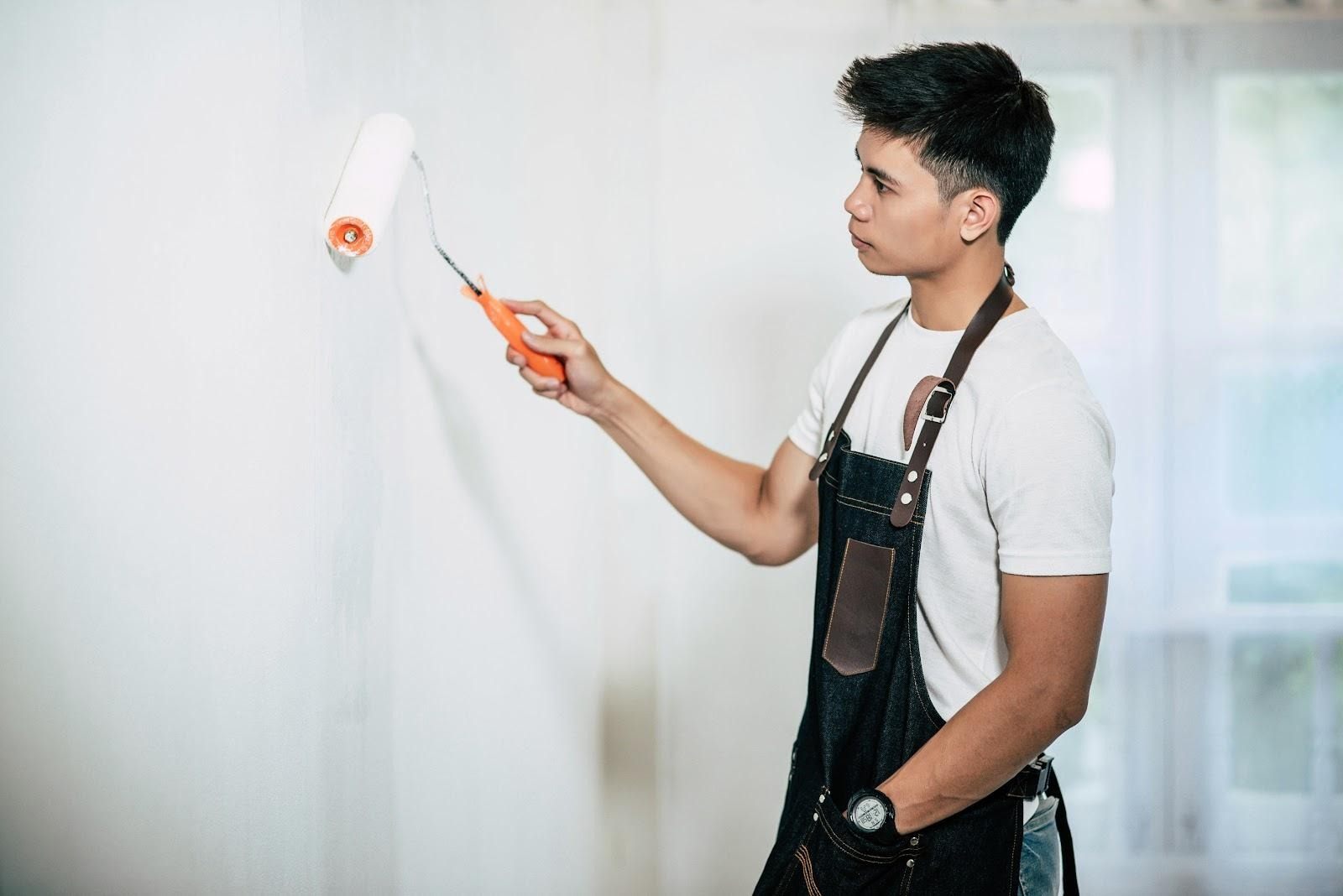 Painter in a work apron rolling white paint onto an interior wall