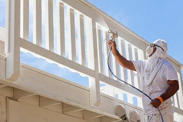 Painter in protective coveralls spraying a white porch railing