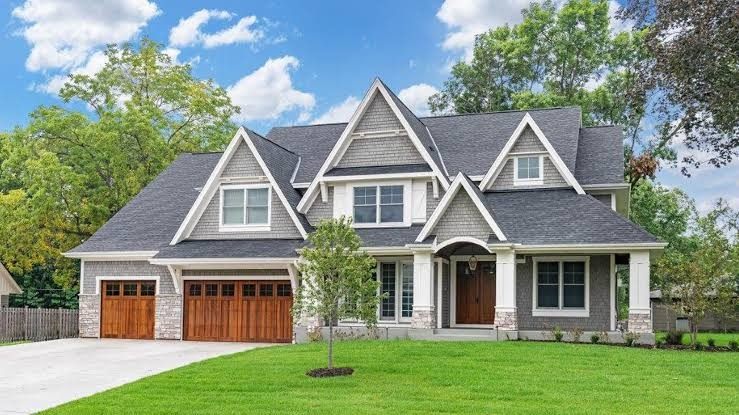 Newly built craftsman house in gray siding and stone, with wooden garage doors