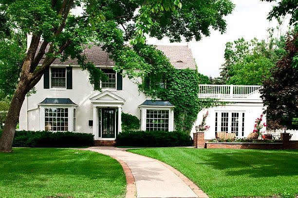 White painted brick colonial house with black shutters and an ivy-covered wing