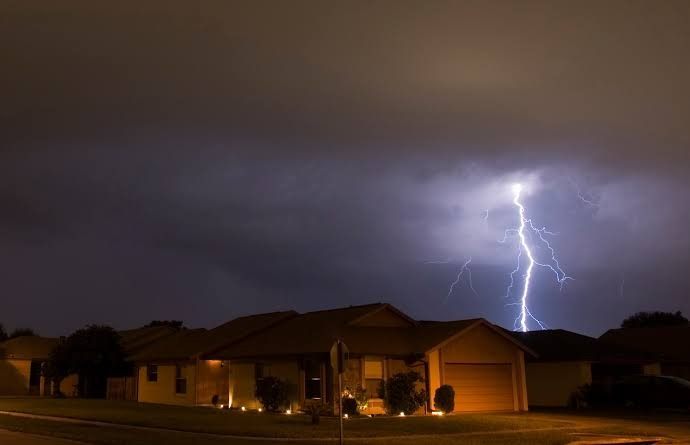 Lightning striking behind a single-story house during a night storm