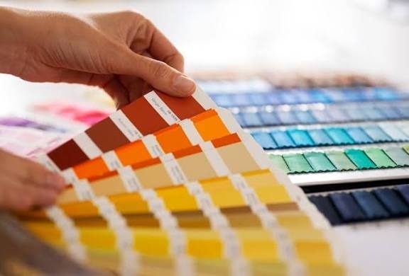 A hand fanning out paint color swatches across a table of sample decks