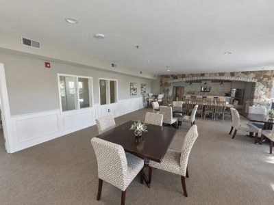 Clubhouse dining room with soft gray walls, white wainscoting and a stone arch kitchen