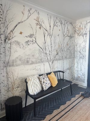 Entry wall covered in a birch forest and mountain mural wallpaper above a black bench with pillows