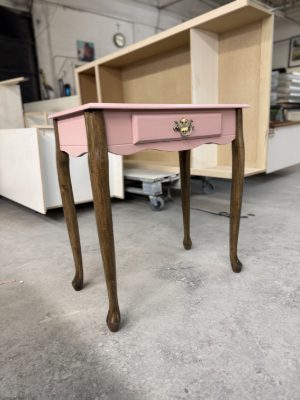 Pink side table with a refinished top and drawer front on stained wood legs, finished in the pre-finish shop
